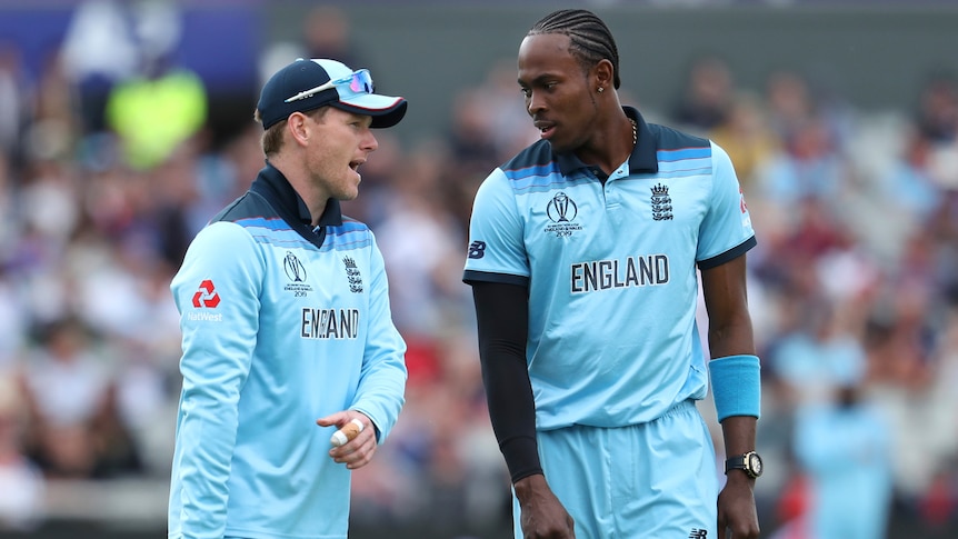 Jofra Archer and Eoin Morgan talk to one another wearing light blue England kit