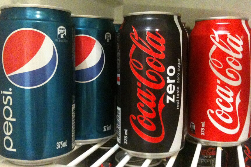 Generic of pepsi, coca-cola zero and original coca-cola sit on a shelf in the fridge.
