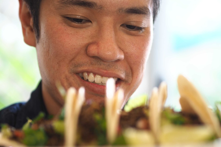 A man smiles behind a plate of tacos.