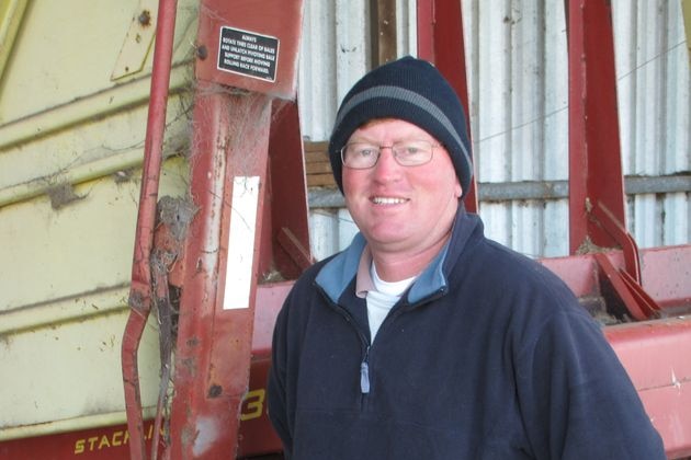 A man in a beanie leans against farm equipment. 