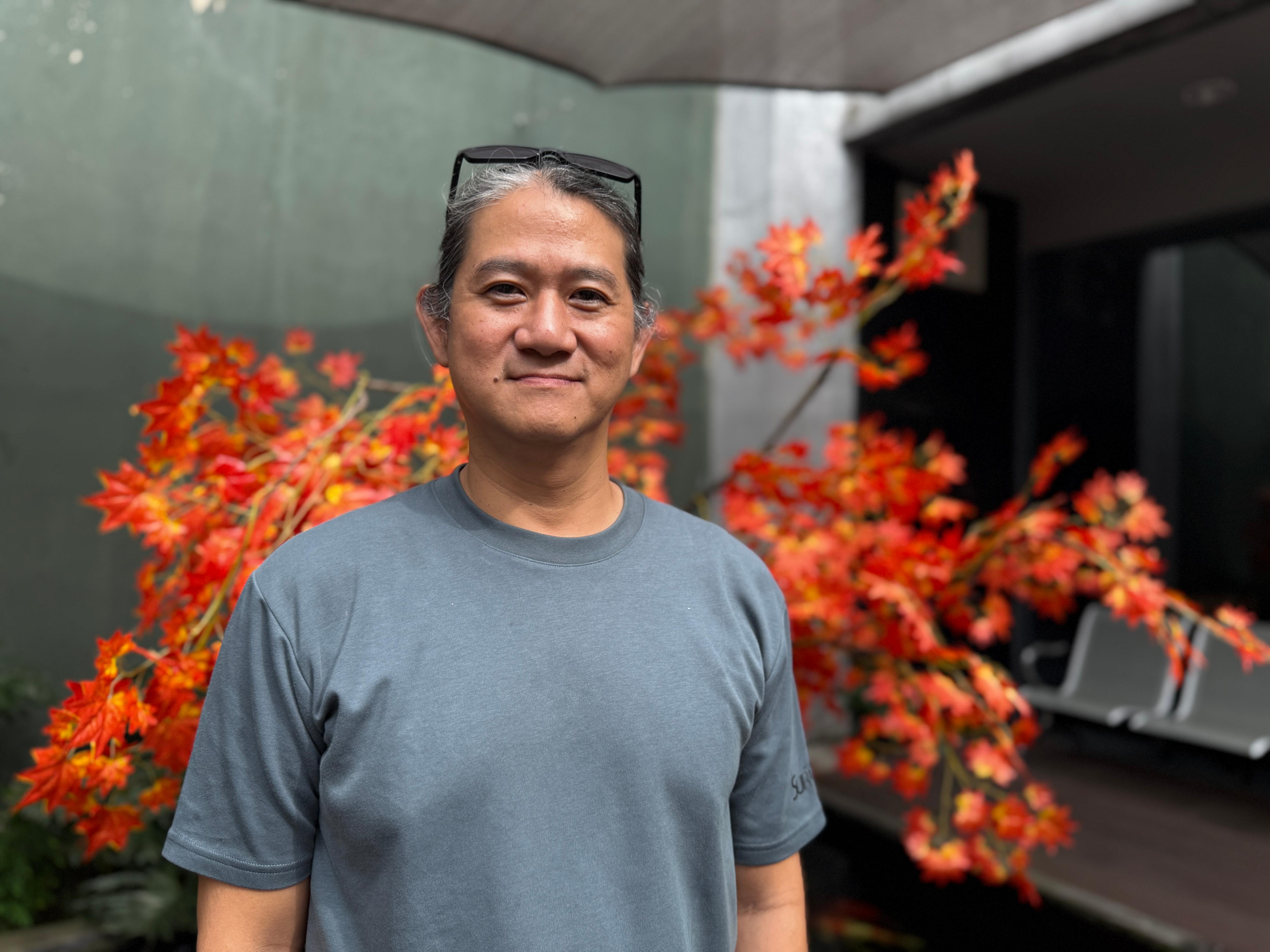 Man in a grey shirt with a pair of glasses on his head smiling to camera.
