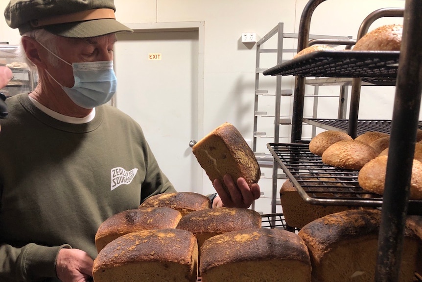 A man with a facemask on looks at sourdough bread loaves. 