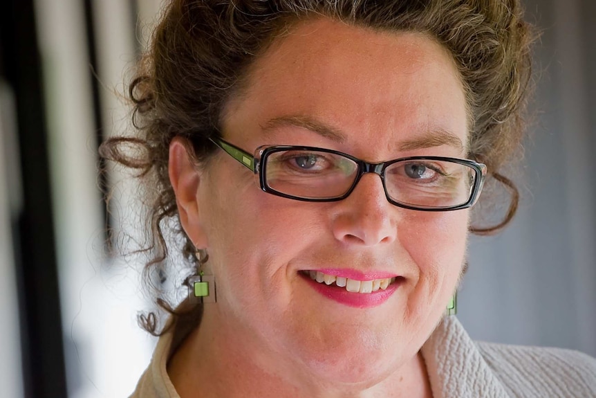 A woman with brown curly hair and glasses smiles at the camera.