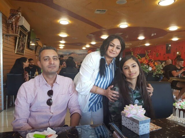 A man sits next to a woman who is affectionately holding the shoulders of a teenage girl, they are sitting in a restaurant