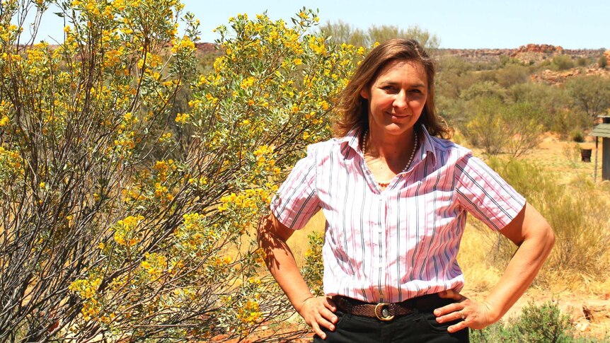 Woman standing beside a wattle bush with hands on her hips.