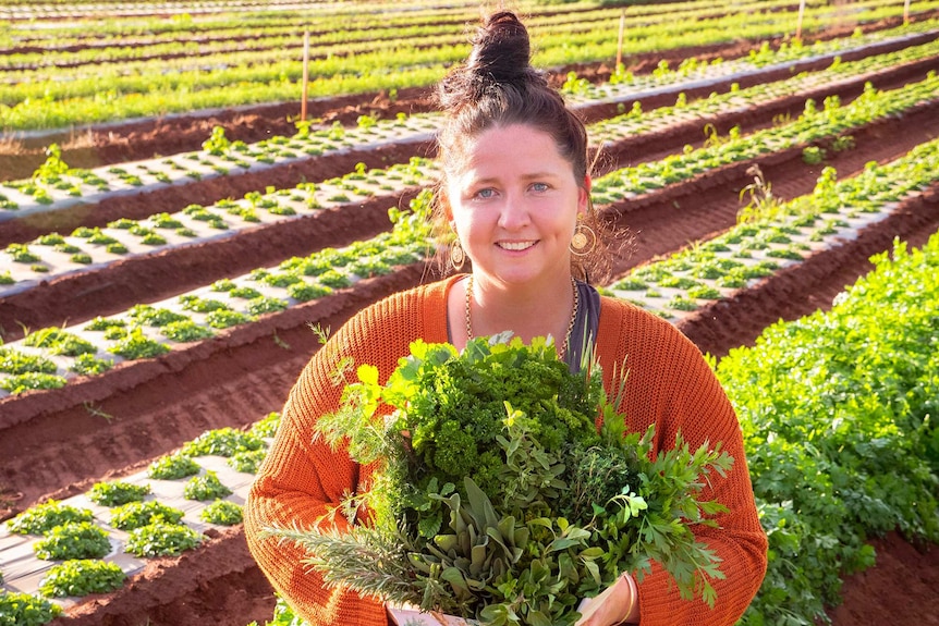 A woman holds a bunch of herbs in a field.