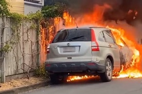 A Honda SUV on fire on a suburban street. 