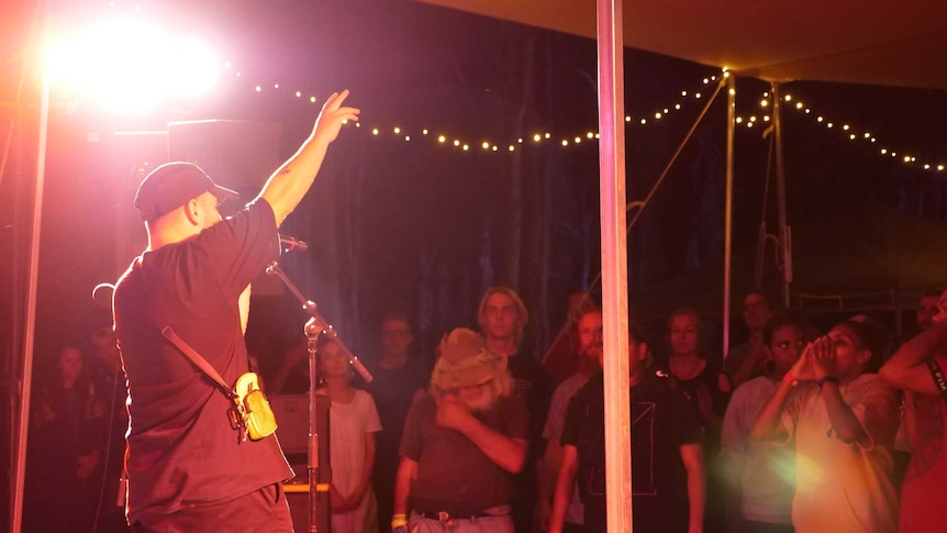 Hip-hop artist on stage with crowd calling out to him.