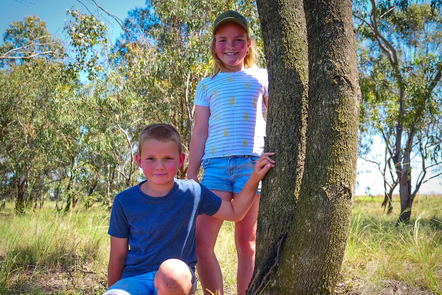 Two children stand beside a tree