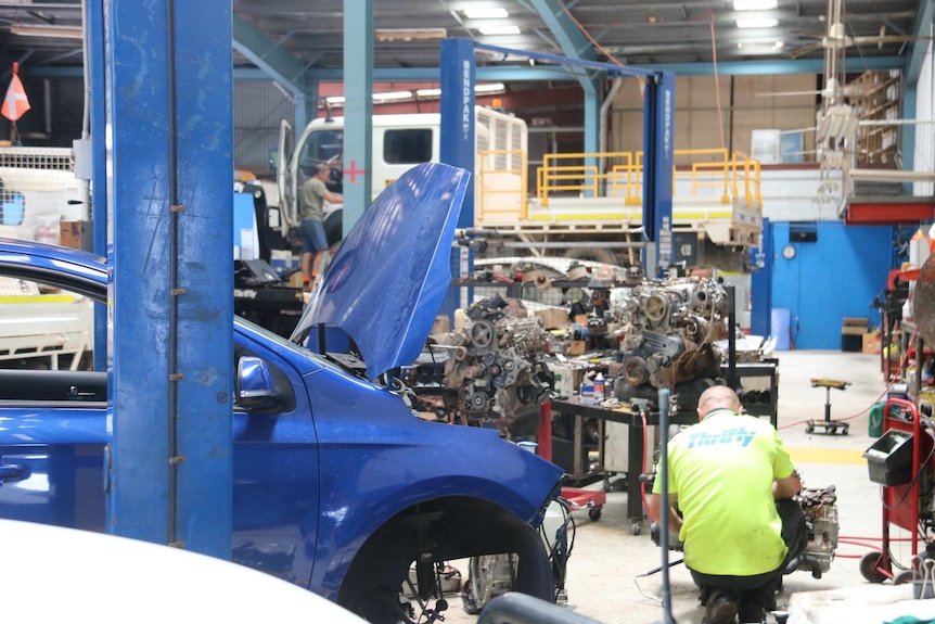 A car with its bonnet popped inside a workroom, surrounded by machinery