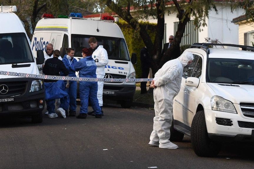 Six police and forensic officers standing near police cars outside the Lalor Park house where a 3 year old fatally shot.