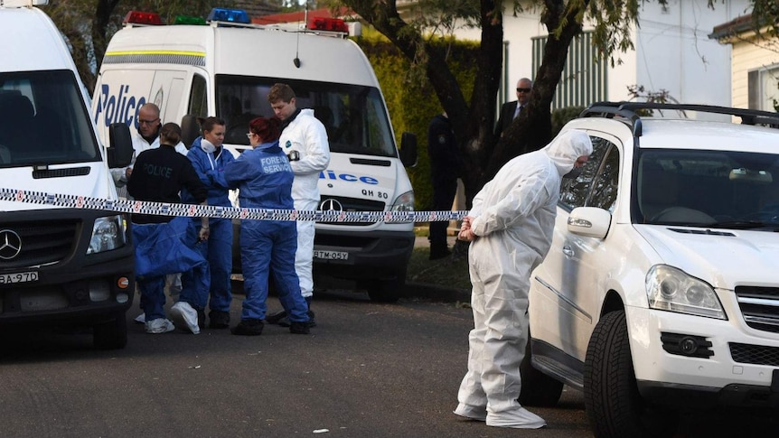 Six police and forensic officers standing near police cars outside the Lalor Park house where a 3 year old fatally shot.