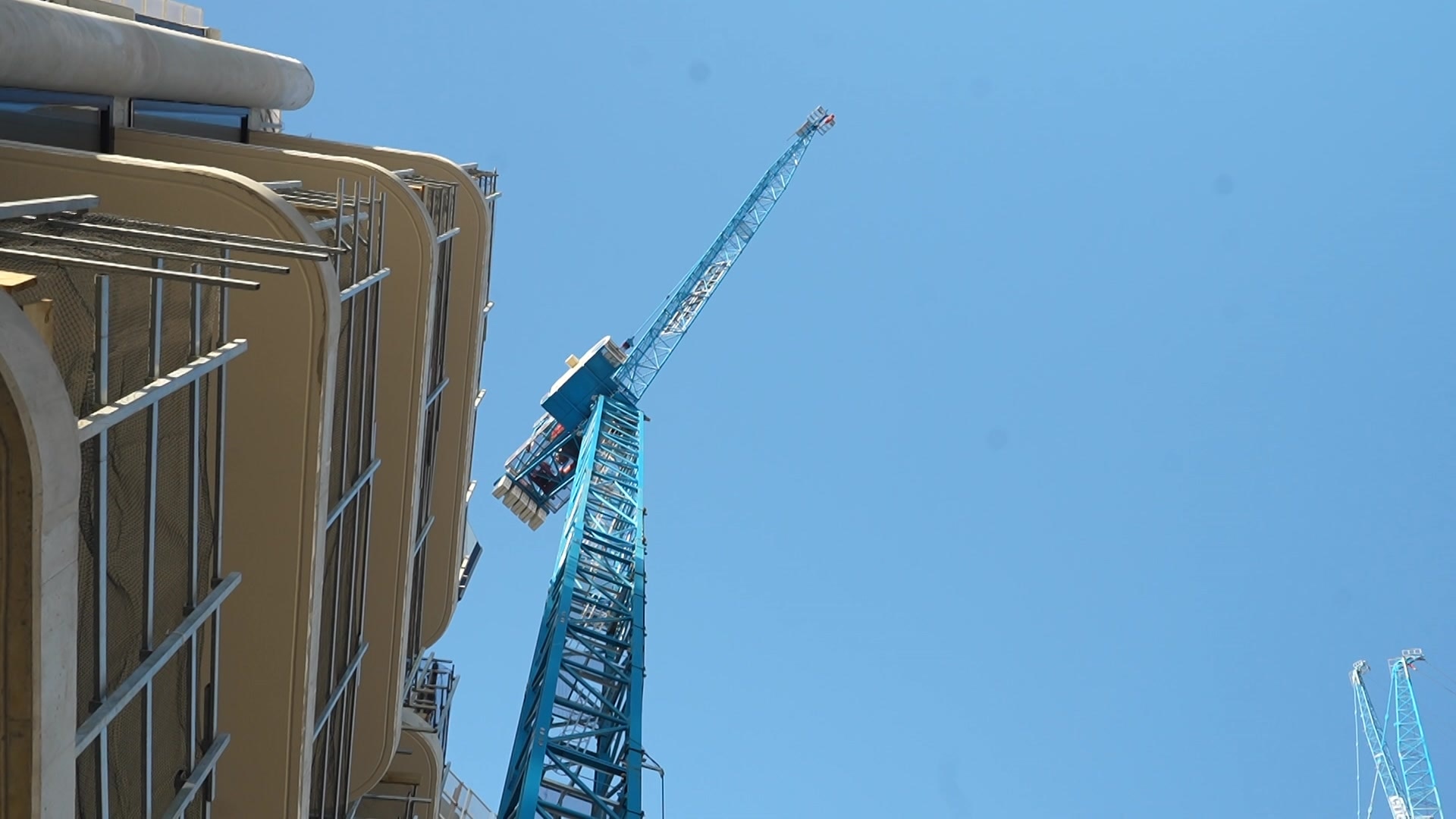 A crane in the sky viewed from ground level, next to a building with scaffolding.