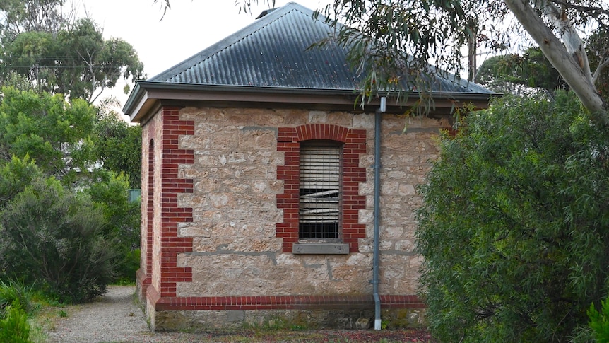 A small 1880s stone building with dilapidated wooden shutters