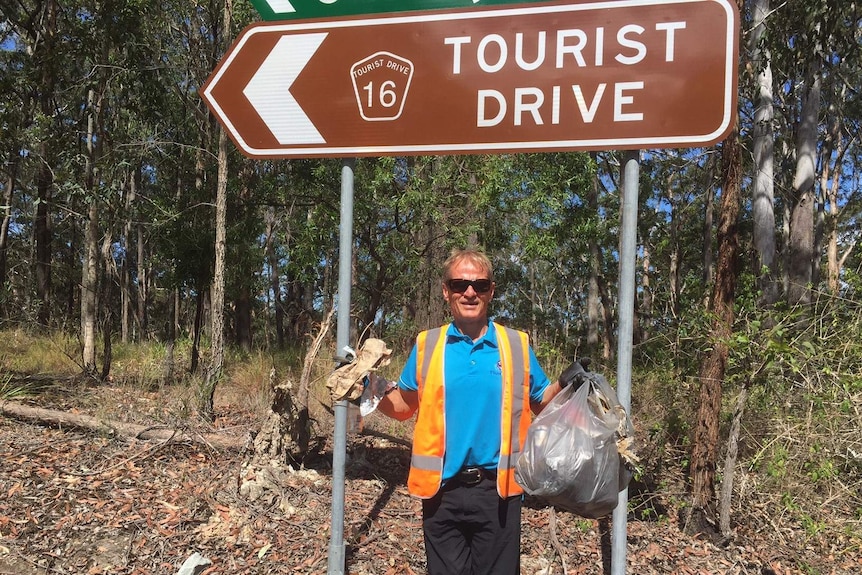 A man holds up a bag of rubbish in front of a sign along the Pacific Highway at Hungry Head.