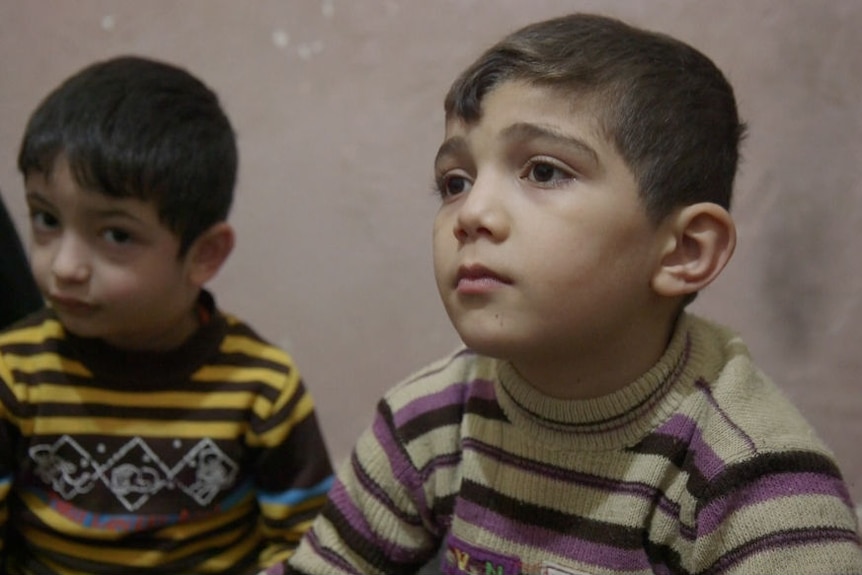 A little boy looks sad as he sits in his family's derelict apartment