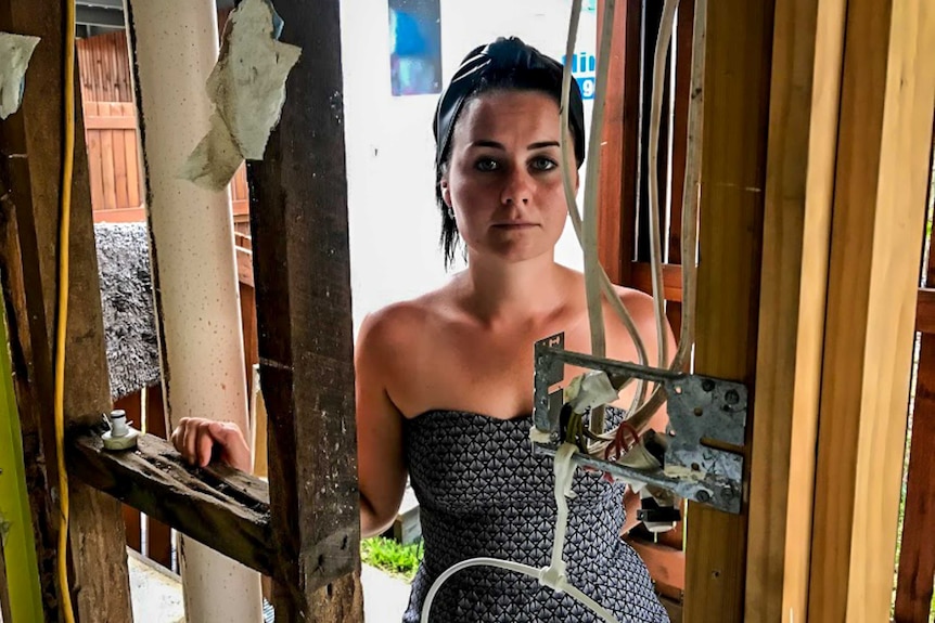 Woman standing in destroyed house with wooden frame and wiring visible