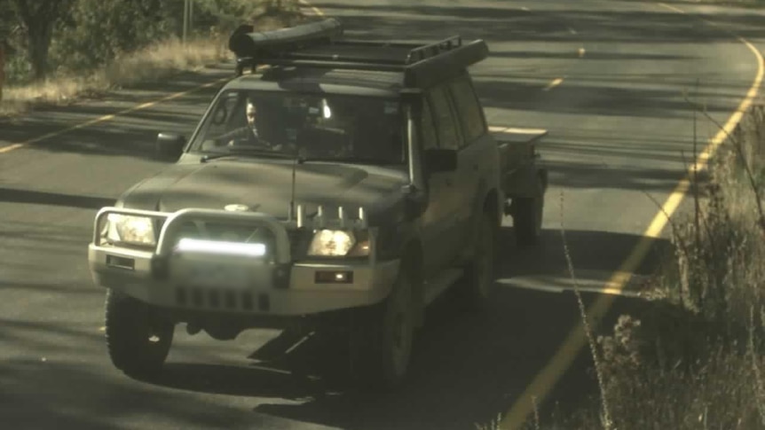 A grainy photo of a four wheel drive driving down a road.