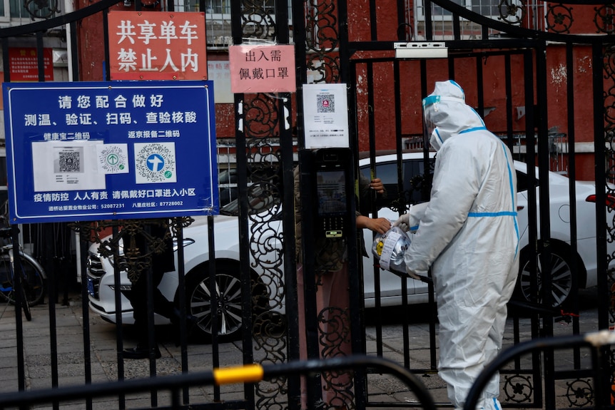A worker in a protective suit passes a delivery good to a resident through a gate of residential compound.