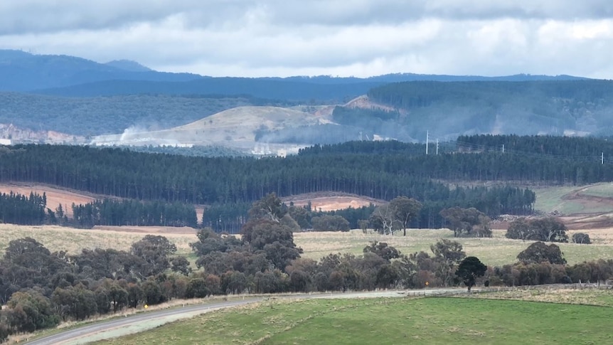 Dust rises off a distant mine site in a rural area.