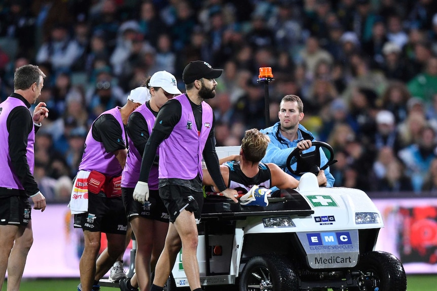 An injured AFL player raises his head as he is taken off Adelaide Oval on a motorised cart.