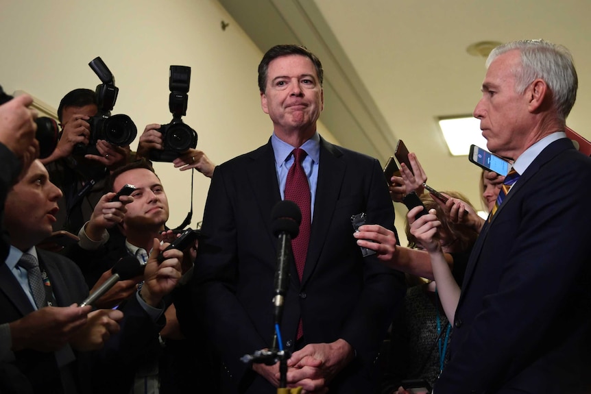 Former FBI Director James Comey surrounded by journalists.