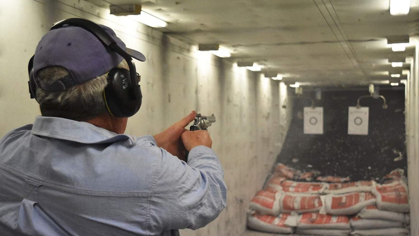 Anonymous man wearing ear muffs holds a pistol preparing to fire the gun at a shooting range