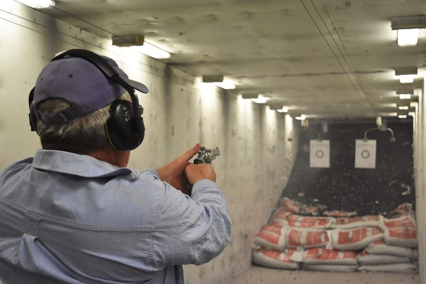 Anonymous man wearing ear muffs holds a pistol preparing to fire the gun at a shooting range