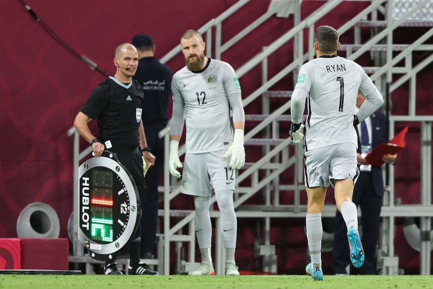 Socceroos goalkeeper Mat Ryan walks off the ground with his back to camera as Andrew Redmayne waits to come on in a vital game.