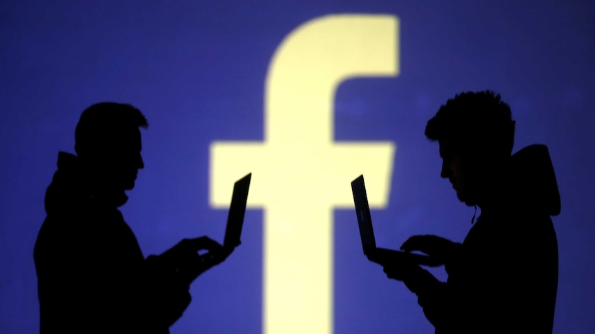 Silhouette of two people using laptops in front of the Facebook logo.