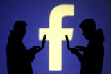 Two men use laptops against a backdrop of Facebook logo