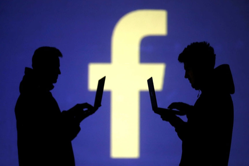Silhouette of two people using laptops in front of the Facebook logo.