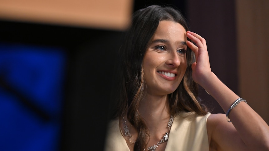 Chanel Contos runs her fingers through her hair on stage a National Press Club. 