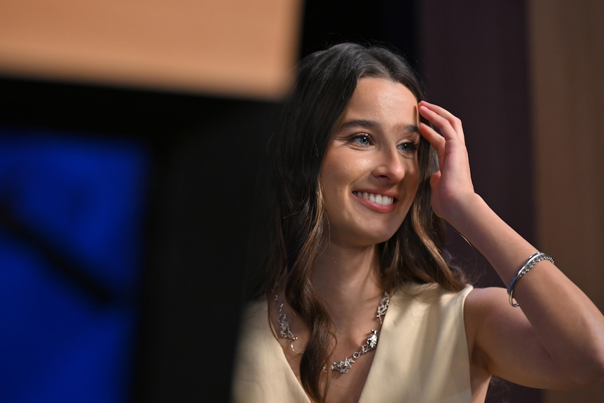 Chanel Contos runs her fingers through her hair on stage a National Press Club. 