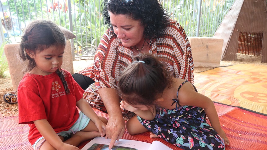 A woman reads a story to two little girls