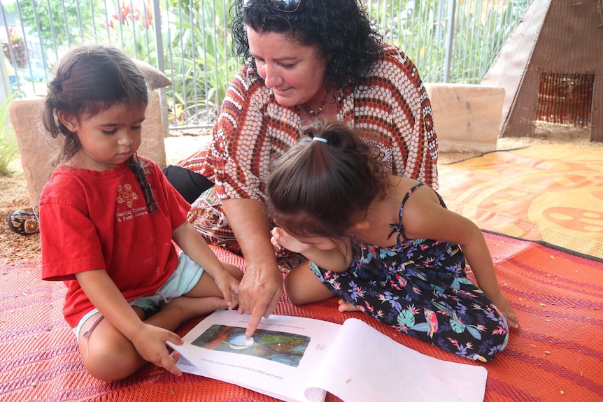 A woman reads a story to two little girls