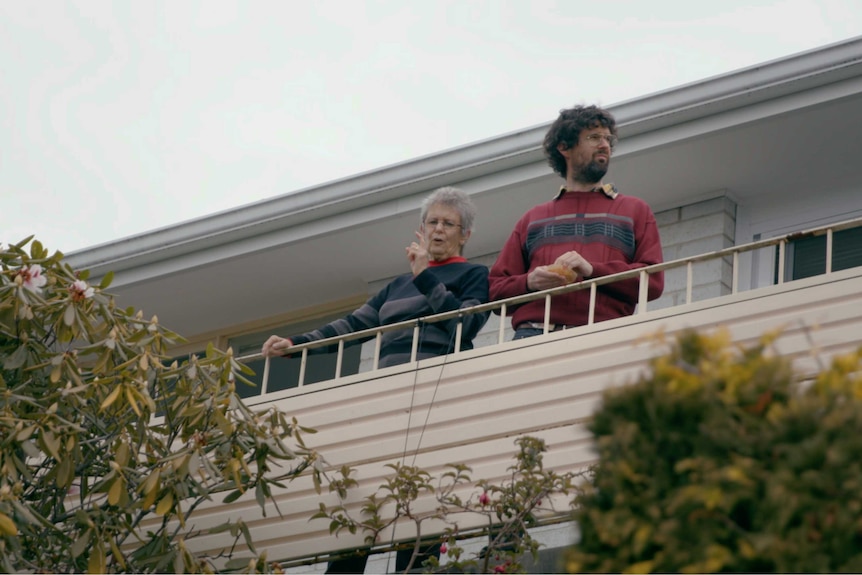 A still from a film of man with his mother standing on the balcony of a house.