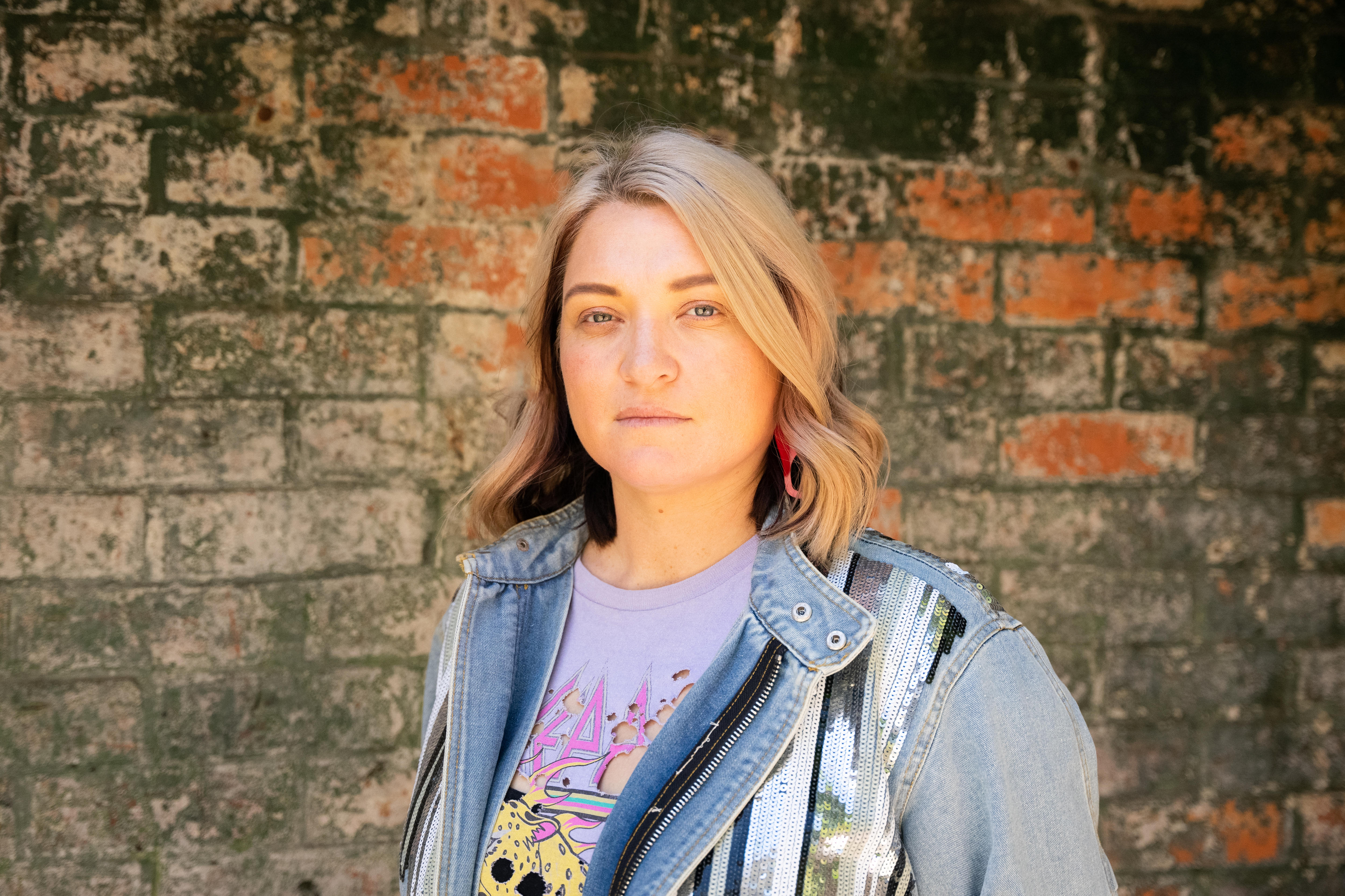 A young woman with shoulder length blond hair was standing in front of a brick wall.