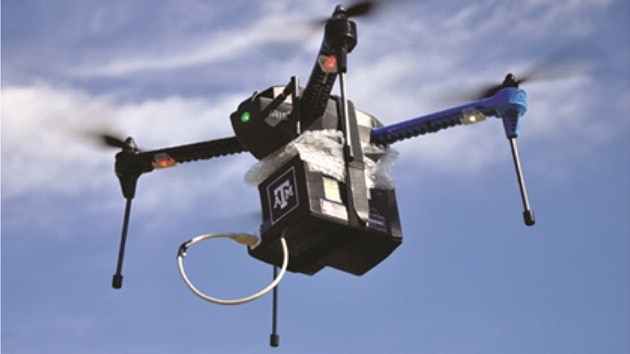 A drone hovers in mid-air, against a blue, partly cloudy sky.