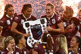 Queensland Maroons lift the Women's State of Origin shield as pyrotechnic flames erupt behind them.