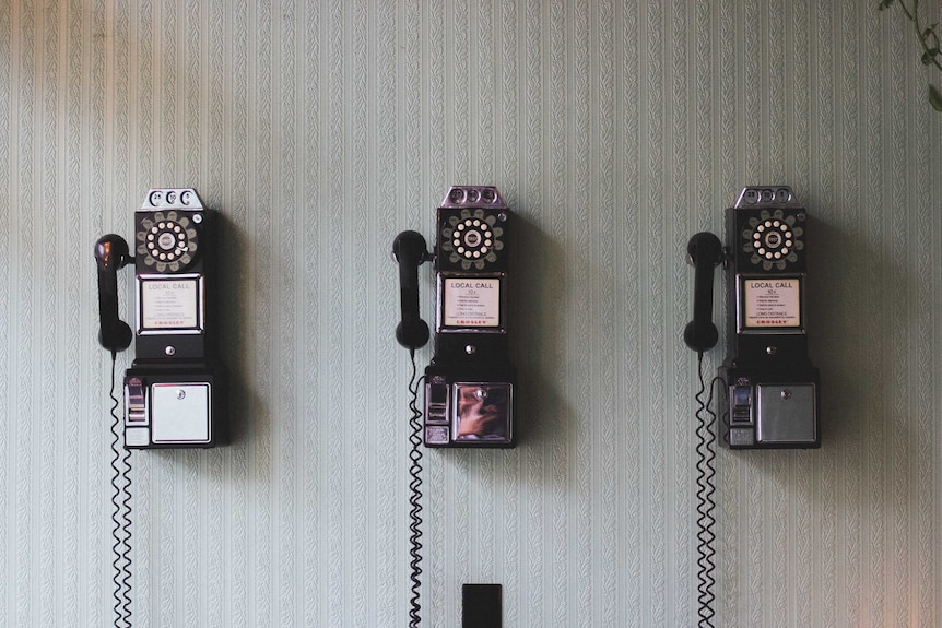 Old style phones hang in a row on a wall.