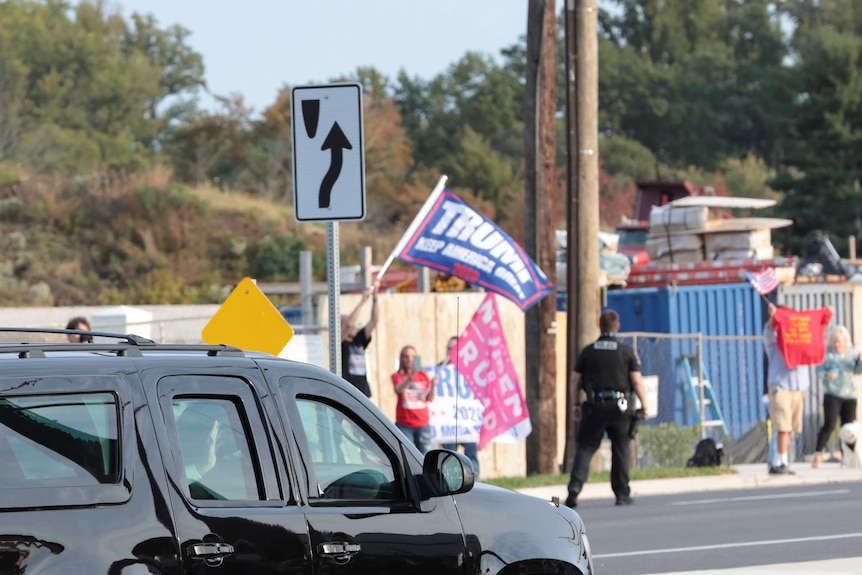 Black car drives by people waving Trump flags