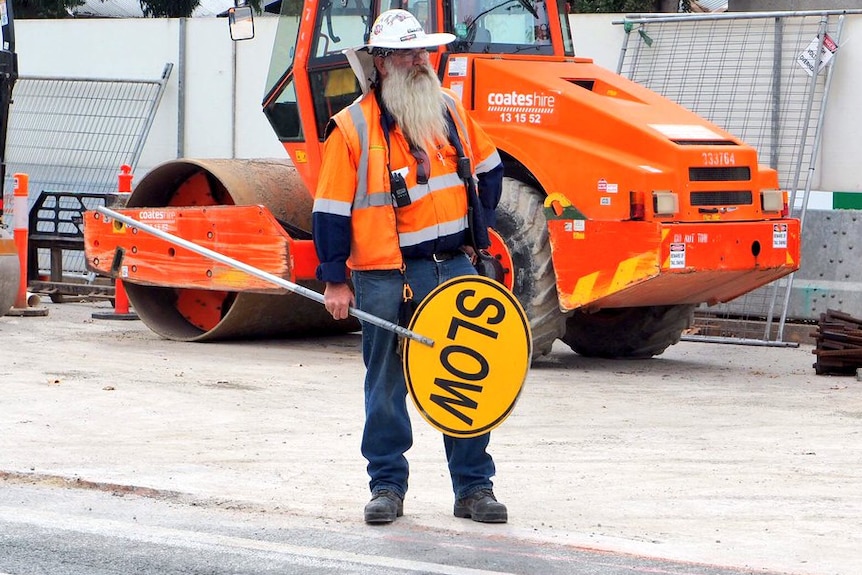 Anthony 'Bear' Sasha stands holding a stop/slow sign at Adelaide roadworks.