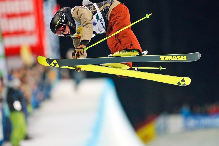 A man in the air on skis, with his torso bent over the fluro yellow skis. 