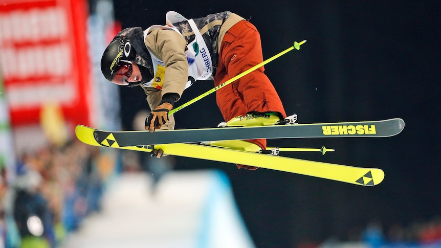 A man in the air on skis, with his torso bent over the fluro yellow skis. 