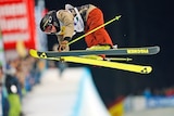 A man in the air on skis, with his torso bent over the fluro yellow skis. 