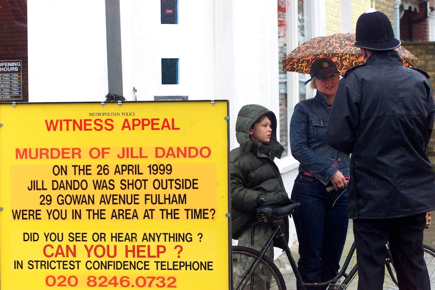 People stand next to a witness appeal billboard 