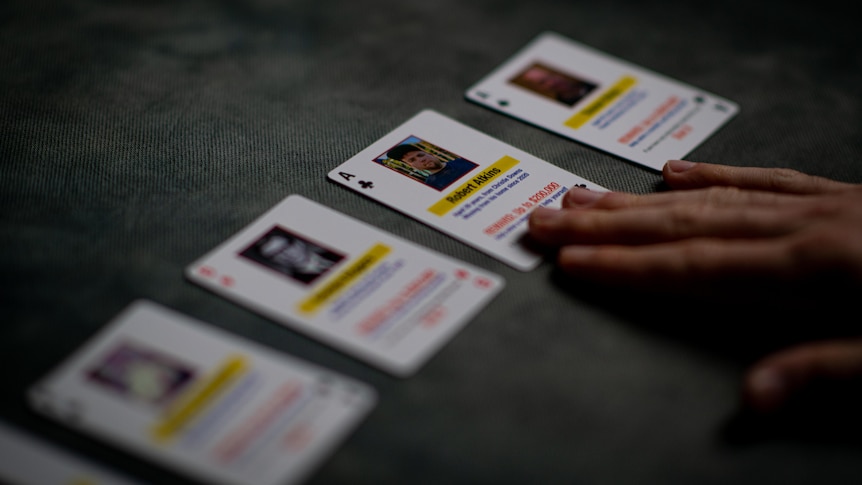 playing cards facing up with photos and words on them as one hand touches one card