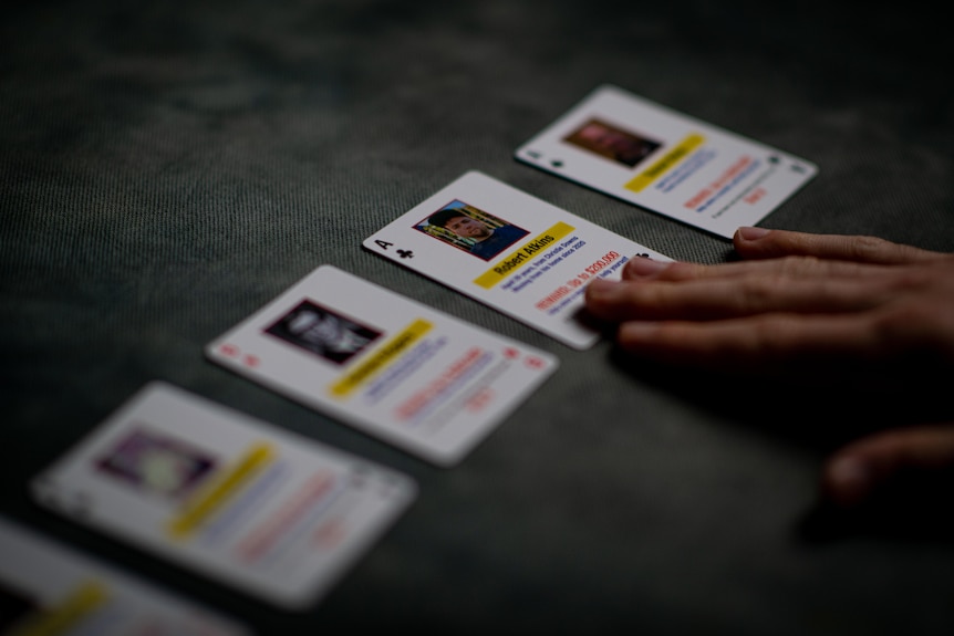 playing cards facing up with photos and words on them as one hand touches one card