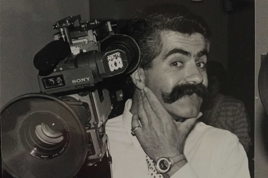 Black and white photo of Vince with big bushy moustache holding camera.